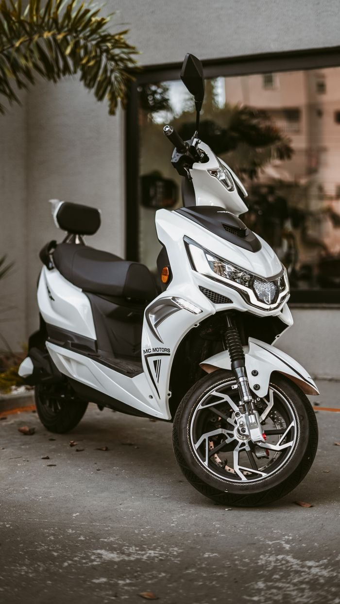 services-02 Sleek white motor scooter parked outside a building with reflections in the background.